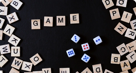 A fekete háttér közepén fából készült betűkockákból a „GAME” szó olvasható, körülötte szétszórt kockák és négy, különböző számokat mutató kocka látható.